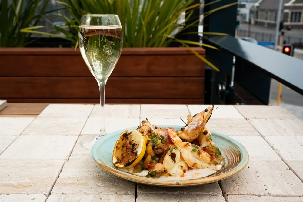 a glass of wine beside grilled prawns